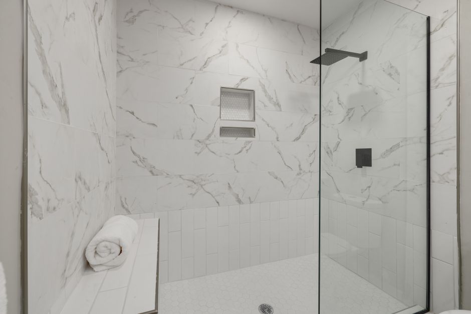 Douche de plain-pied en marbre clair avec banc intégré et paroi vitrée